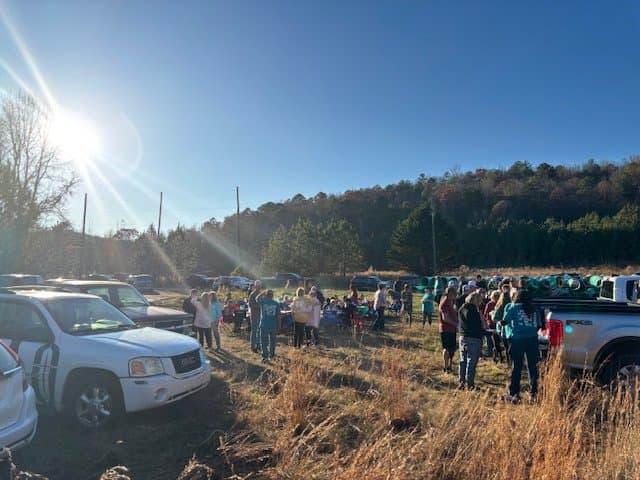 A large outdoor gathering of people in a grassy field under a clear blue sky.