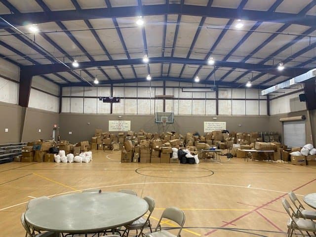 An indoor gymnasium filled with numerous boxes and bags for a donation or distribution event.