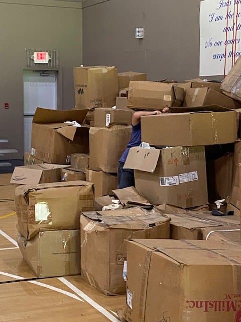 A volunteer behind a stack of large cardboard boxes during a donation sorting event.