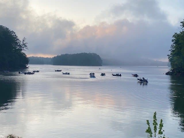A river scene with several boats floating on calm water, surrounded by trees.