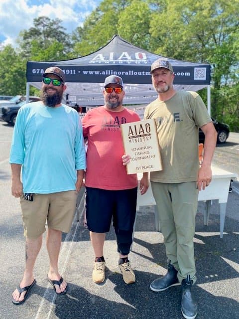Three men holding a plaque that reads AIAO Ministry 1st Annual Fishing Tournament 1st Place.