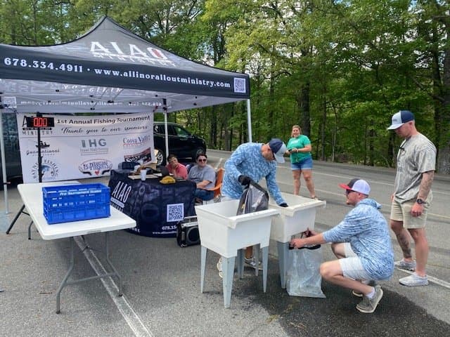 People gathered around fish tanks at an outdoor fishing tournament registration booth.