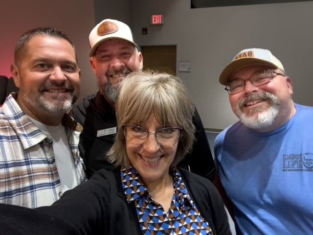 Four smiling adults taking a selfie indoors together.