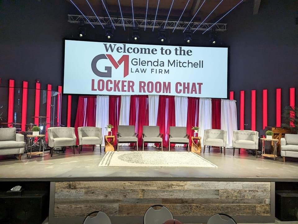Stage setup for a panel discussion with nine chairs and a large screen displaying the Locker Room Chat event title.