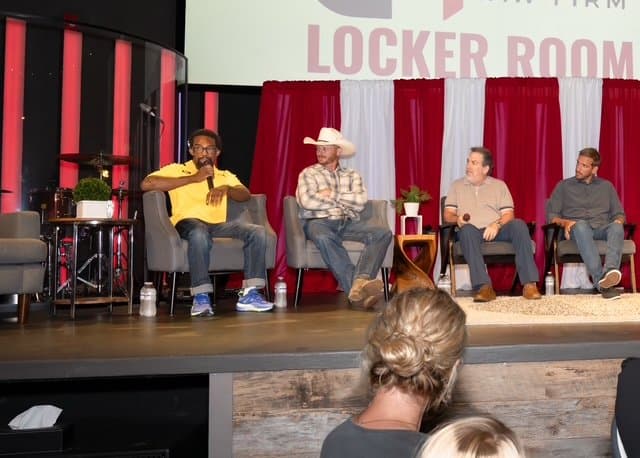 Four men on a panel discussion stage with a backdrop reading Locker Room.