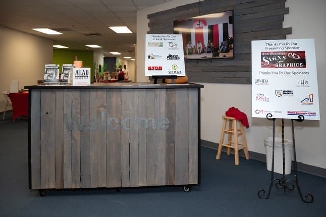 Reception desk with a TV screen mounted on the wall and a sponsor thank-you sign.