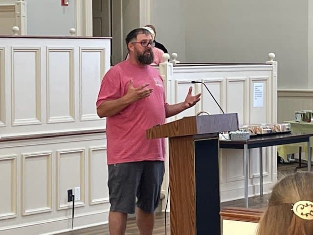 A man speaking at a podium in a room with a table of food.