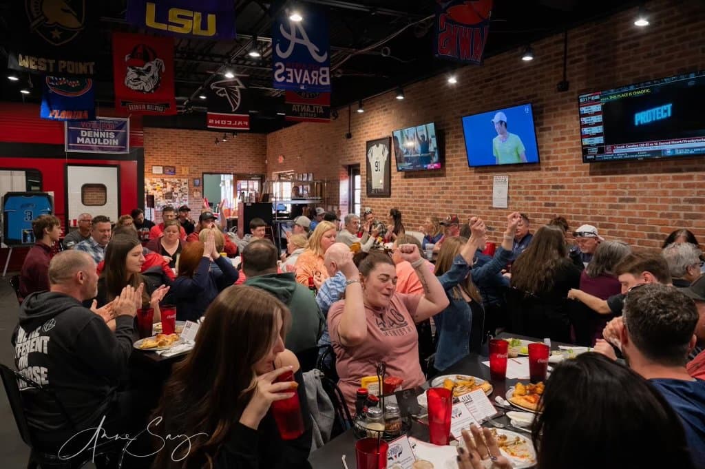 Crowd of people at a sports bar watching television screens and celebrating.