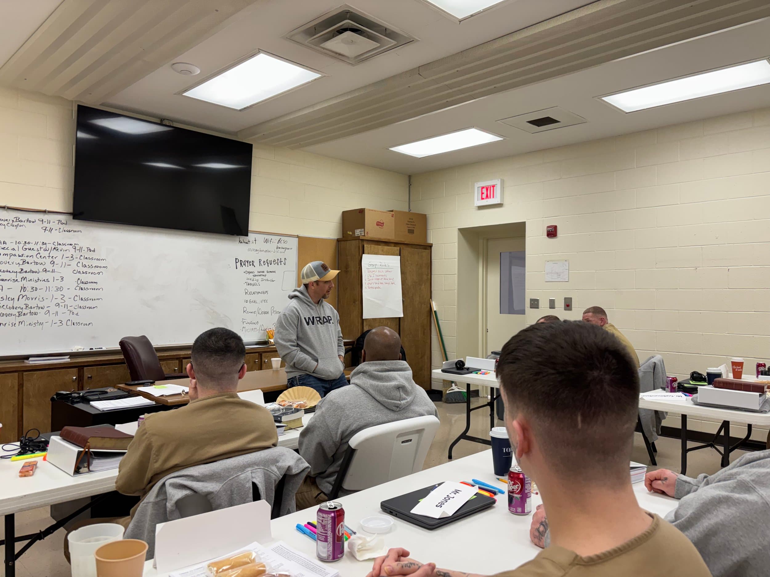 A classroom of students listening to an instructor near a whiteboard